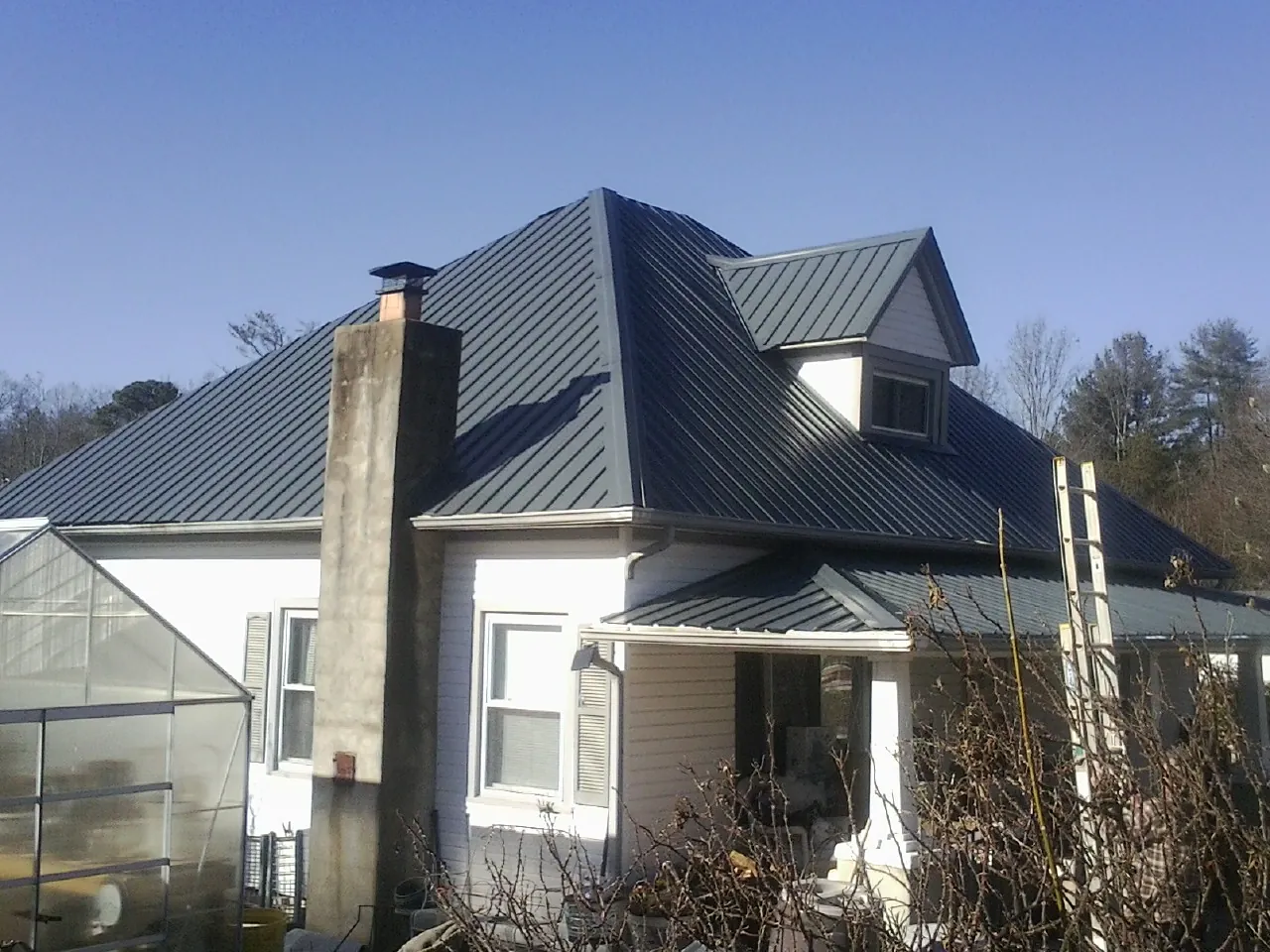 Dark blue standing seam metal roof on a white farmhouse with dormer — Slate & Tile Roof Repair by Roofing Brothers in Bitely