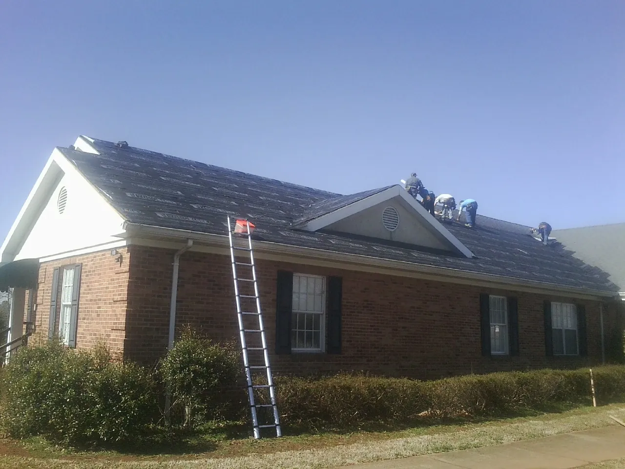 Crew tearing shingles off a brick ranch roof with a ladder set — Emergency Roof Repair work by our crew in Bitely