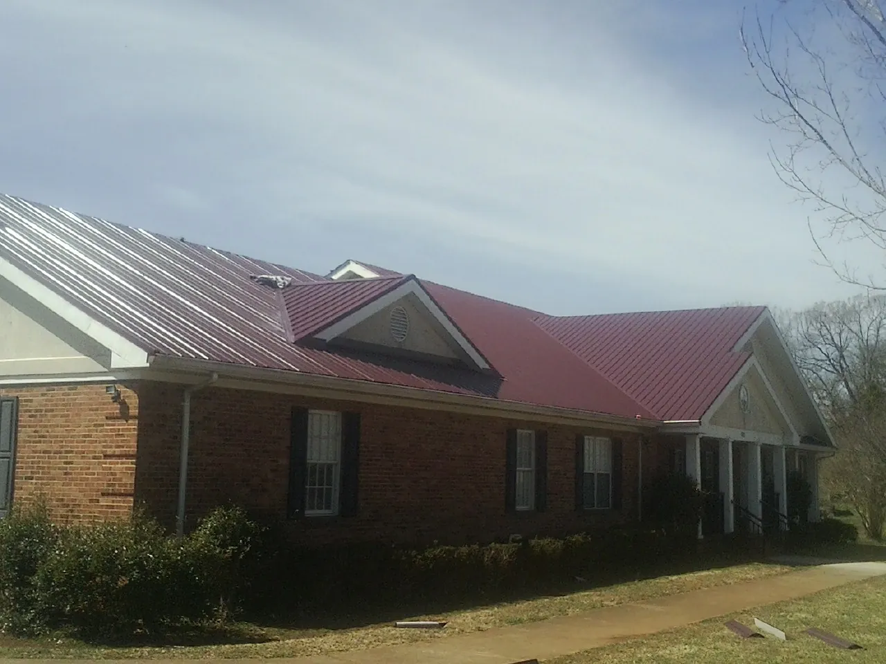 Red metal roof with gabled entries on a long brick building, from a Hail Damage Roof Repair job in Bitely