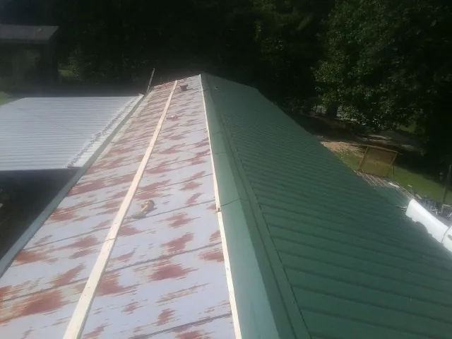 Old rusted panels beside newly installed green metal roofing — Wind Damage Roof Repair by Roofing Brothers in Bitely