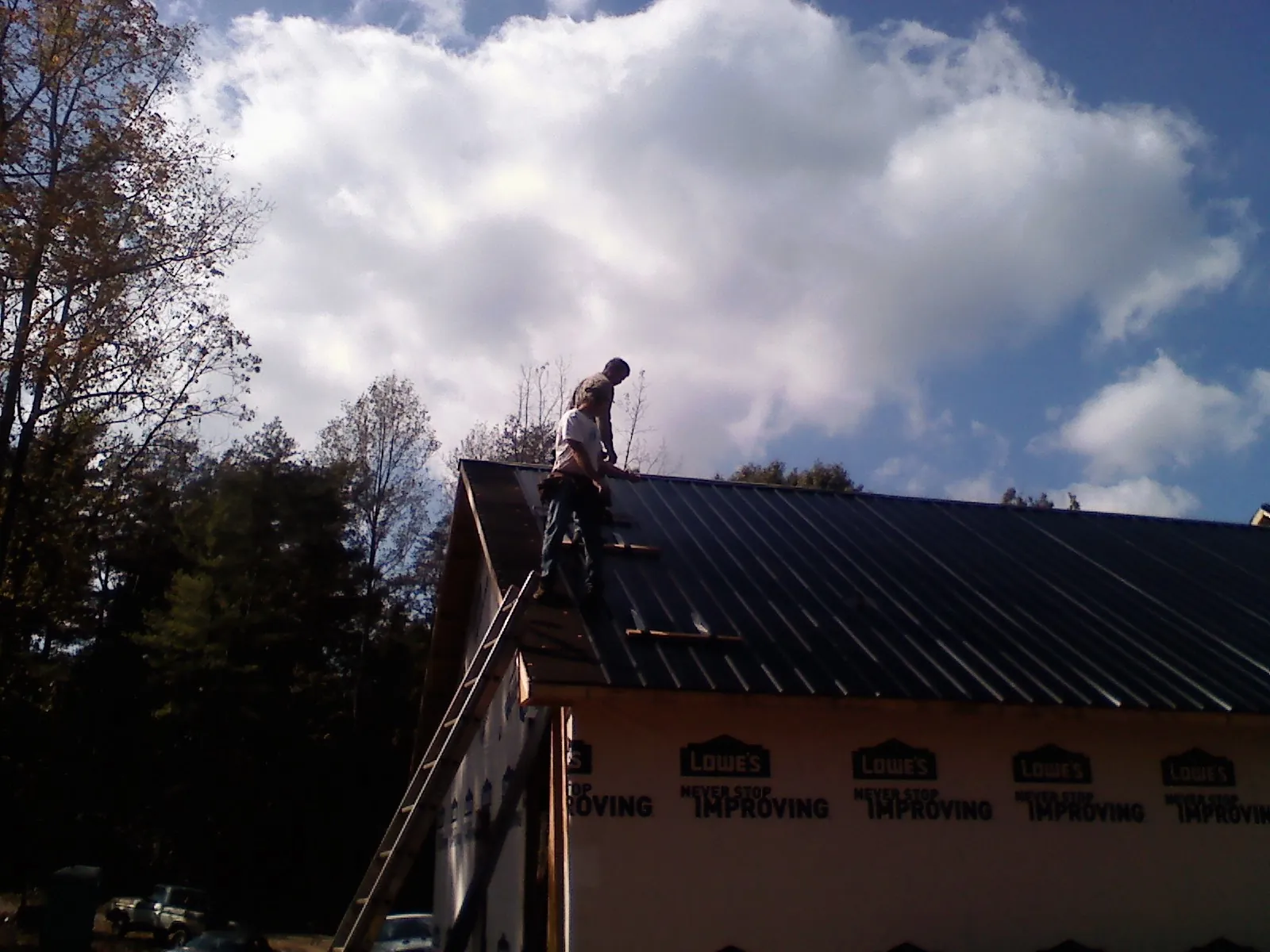 Roofer fastening dark metal panels high against a cloudy sky, from a Roof Inspection job in Bitely